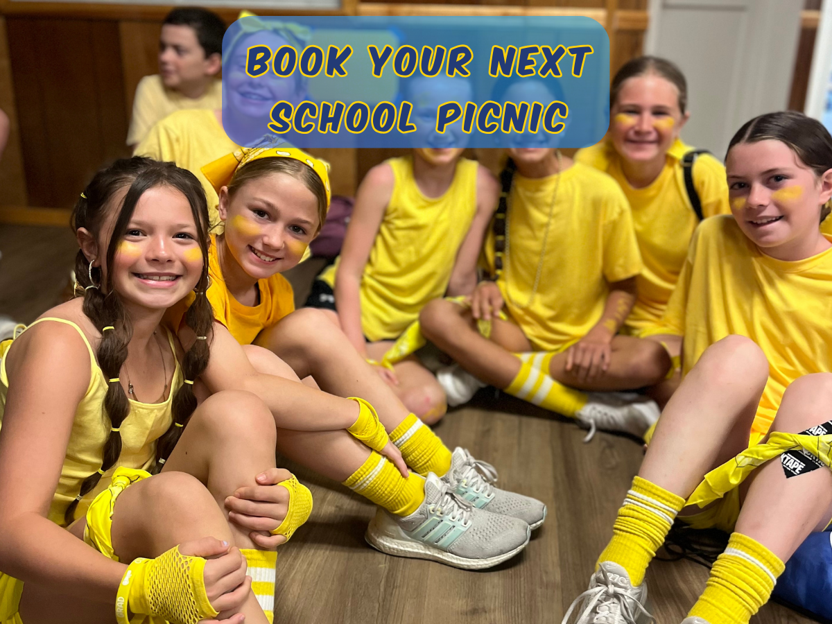 Students wearing yellow shirts sit together smiling during a school graduation picnic at Rolling River Day Camp.